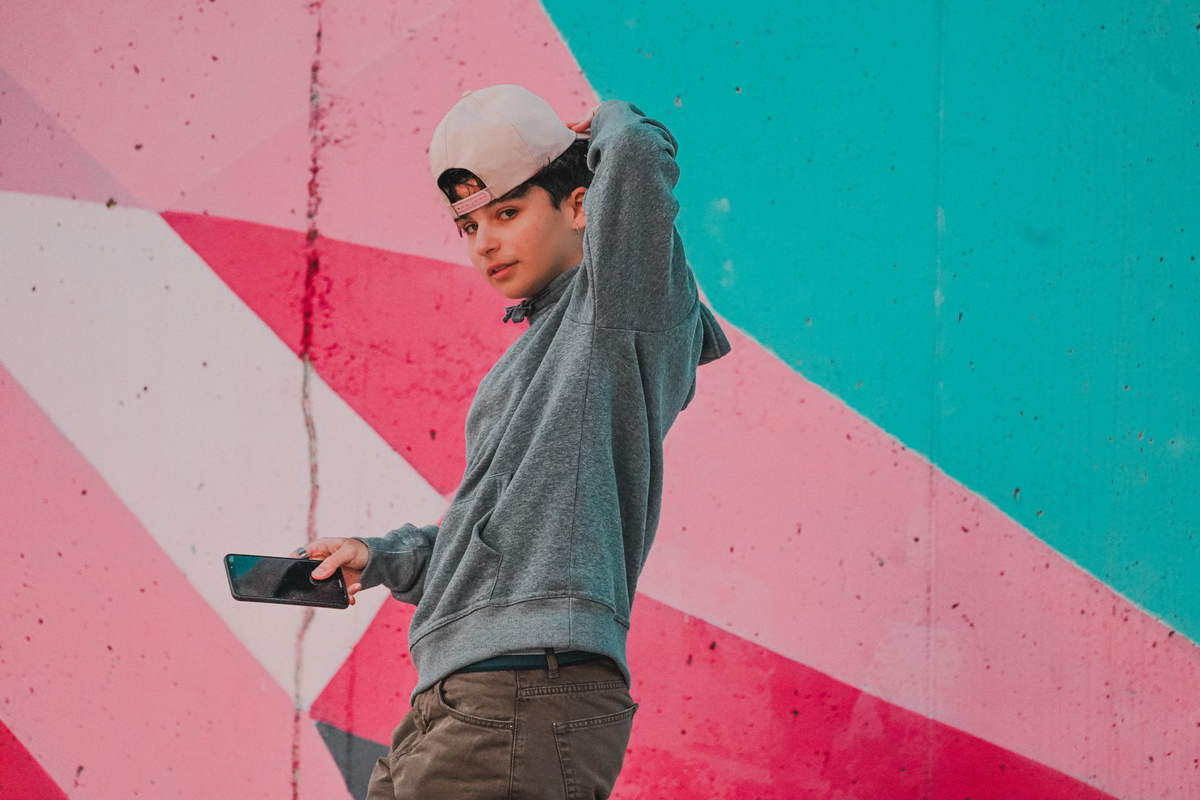 Stylish adolescent with smartphone near bright wall